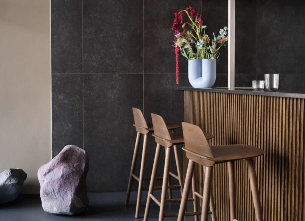 A modern interior featuring a dark stone wall & wooden high stool.