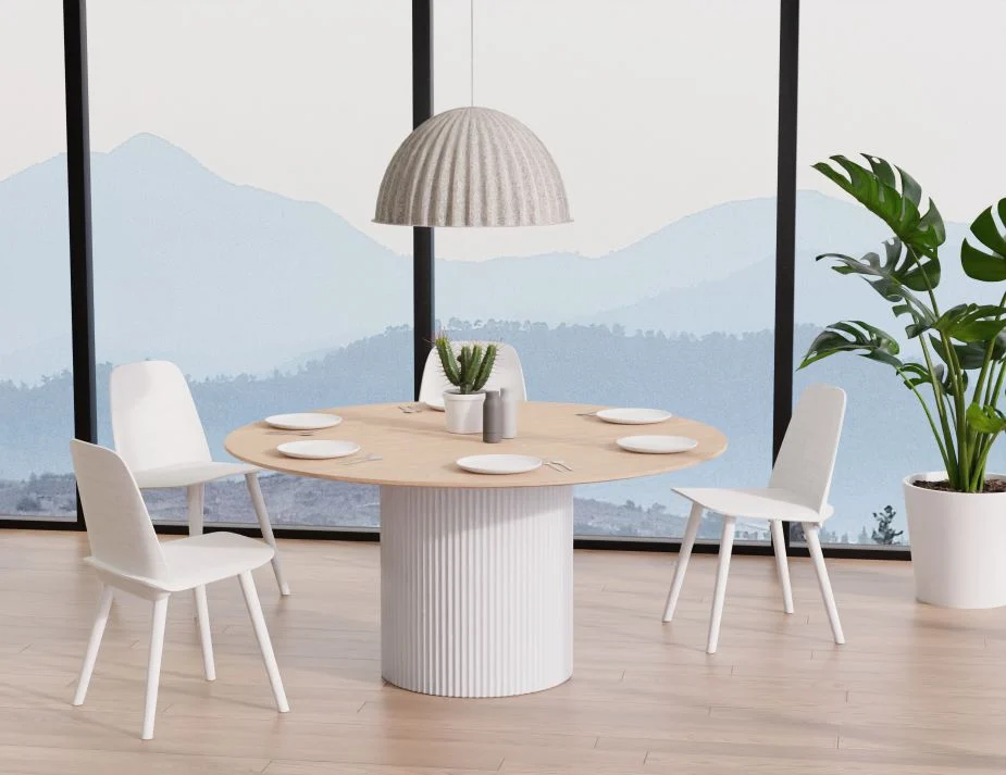 A minimalist dining room with large windows showcasing a mountainous view. The central focus is a round wooden table with a ribbed base, complemented by sleek white chairs. The table is set with light gray plates, silverware, a white potted succulent, and other table accessories. A white pendant lamp hangs above, and there's a tall green potted plant by the window.




