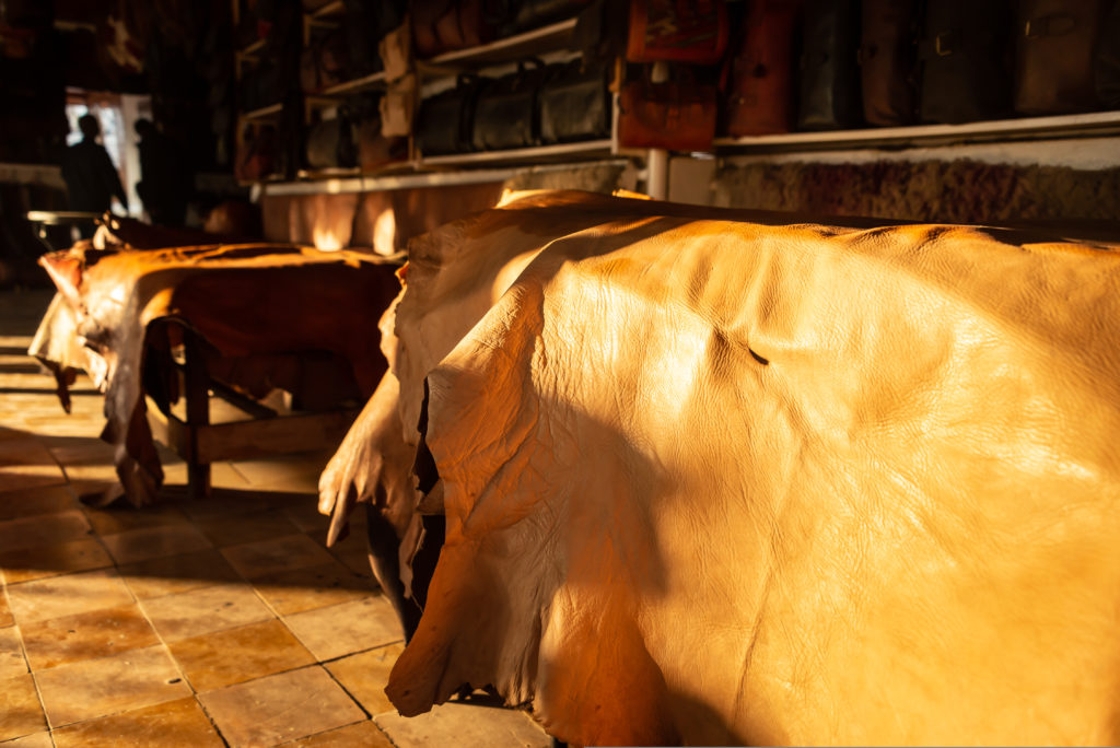 Piles of leather displayed in warm sunlight, showing different colours and textures, with leather goods visible in the background.