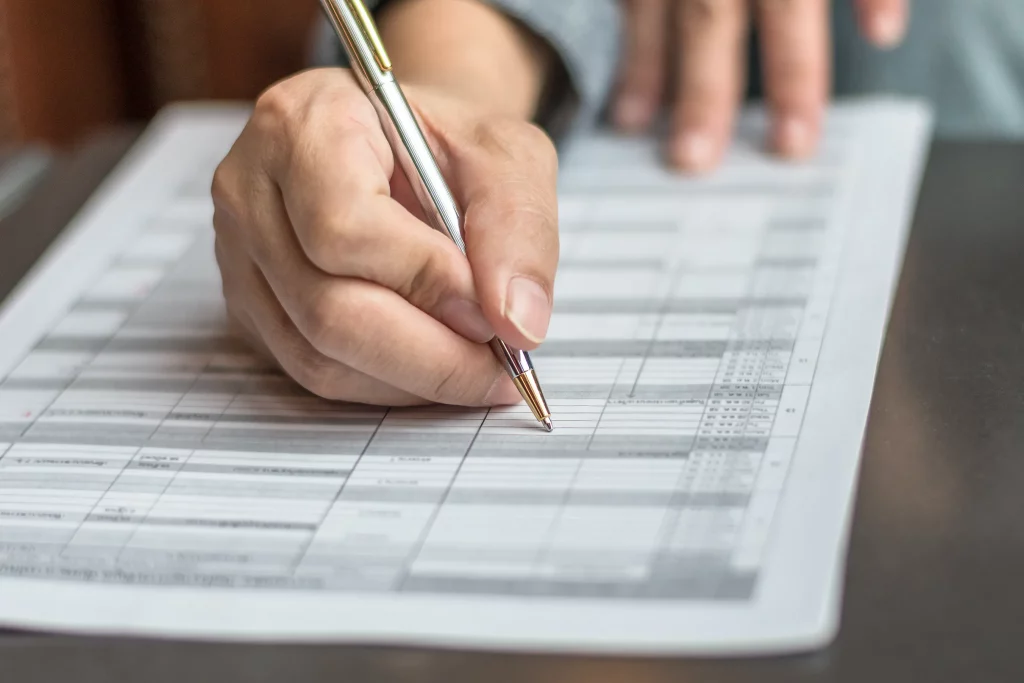 Close-up of a person's hand holding a pen, poised to fill out a printed form.