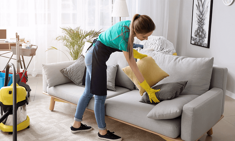 Housekeeper fluffing pillows on a sofa.