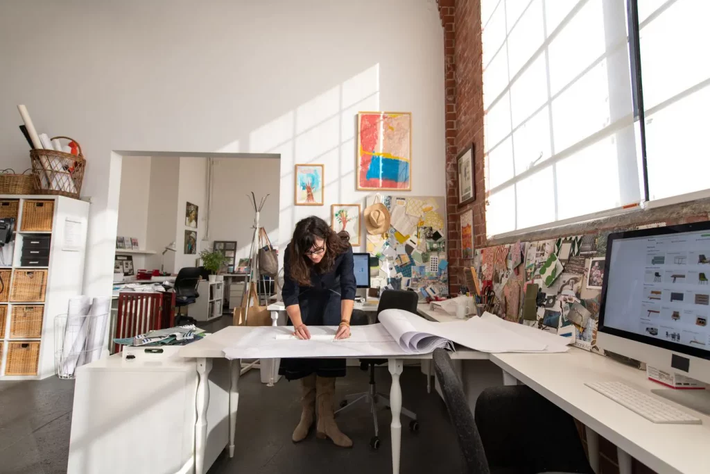 A home designer in an office space, leaning over a desk.