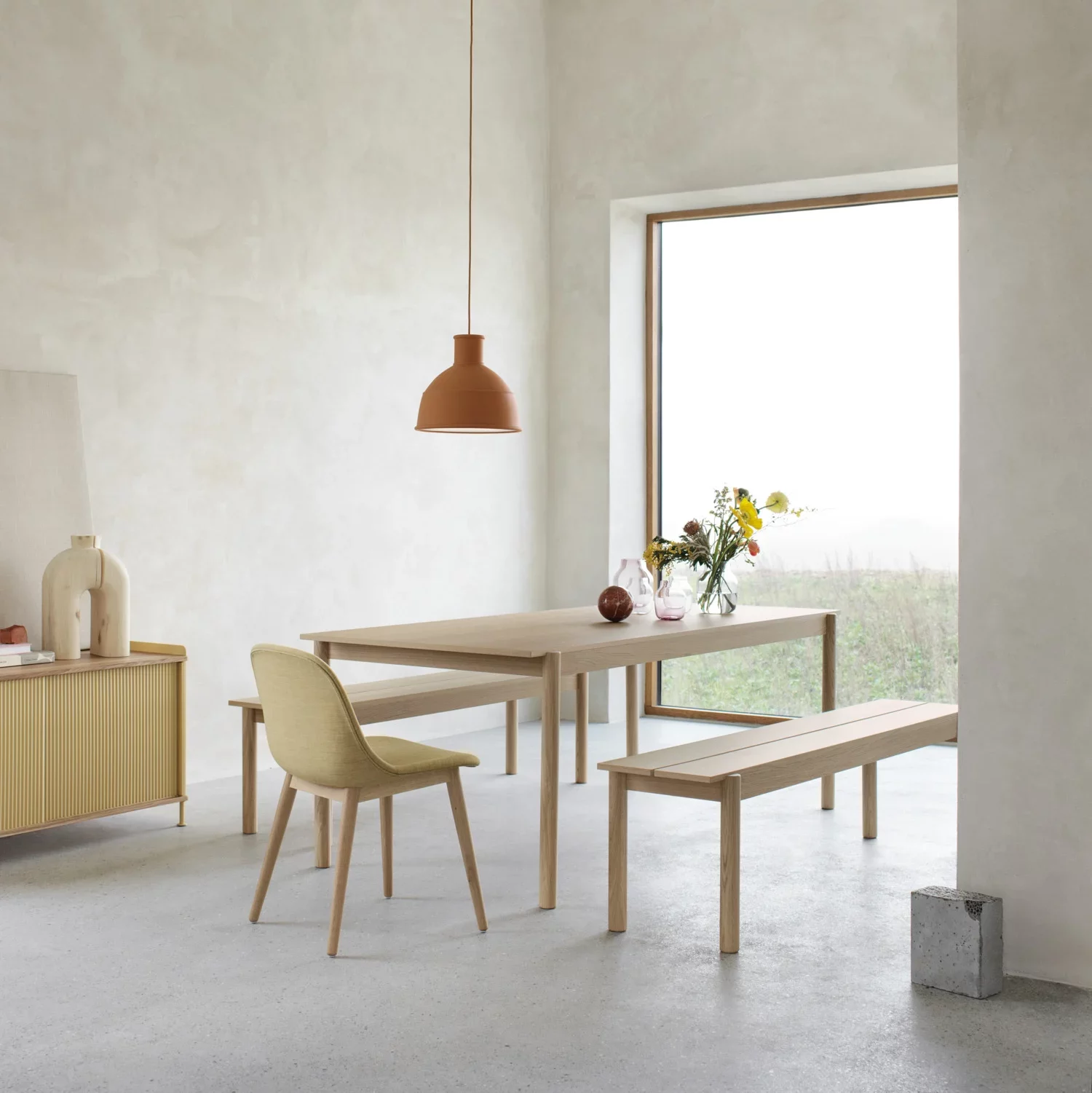 Minimalist dining area with light wood furniture and terracotta pendant light.