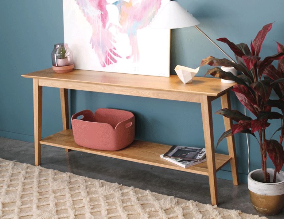 A modern wooden console table against a teal wall.