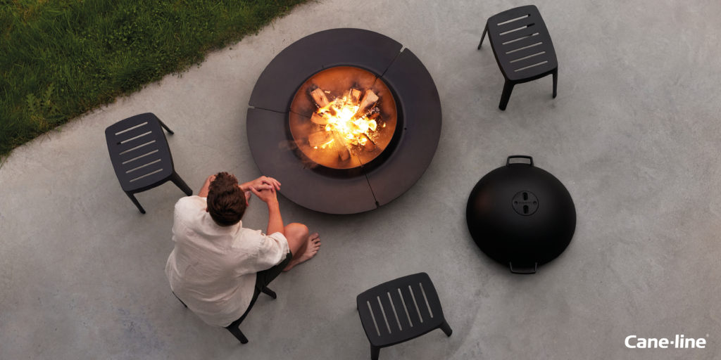A person sitting next to a Cane Line fire pit.