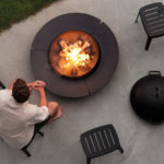 A person sitting next to a Cane Line fire pit.