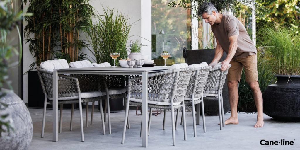 A man adjusts a chair around a Cane-line dining set.