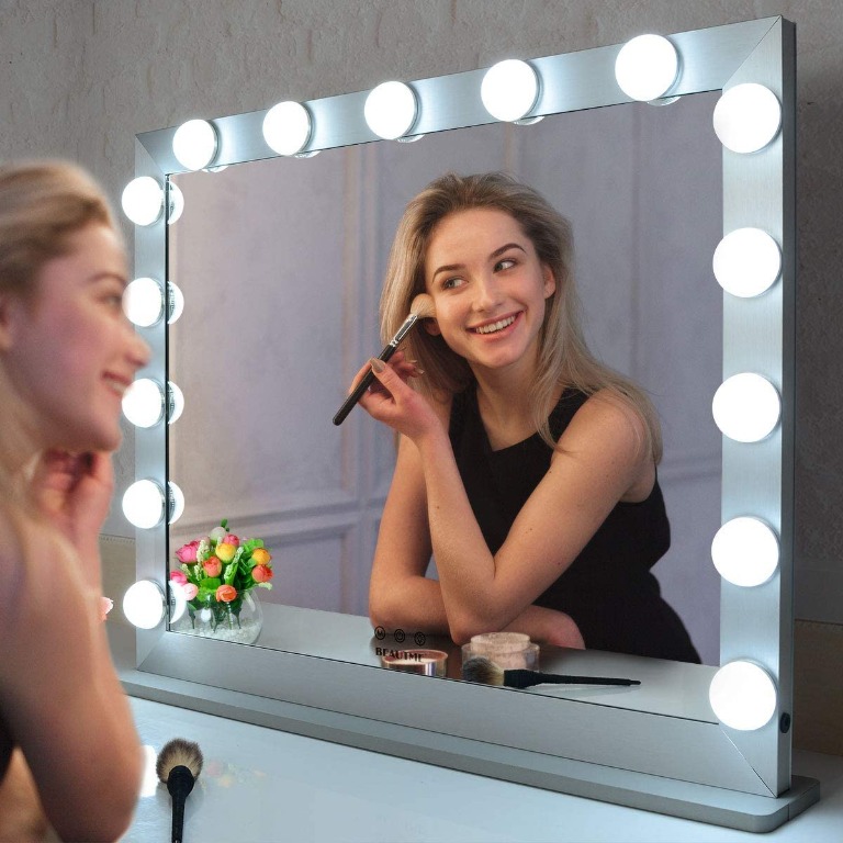 Young woman applying blush while looking vanity mirror.