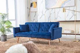 A vibrant and cozy setting dominated by a deep blue velvet sofa with button tufting. The sofa is placed against a backdrop of white walls adorned with abstract art, and a beige shaggy rug adds warmth to the floor.