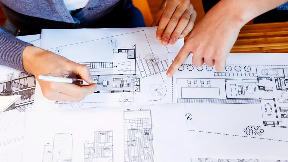 Close-up of hands pointing on detailed architectural blueprints.