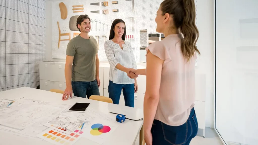 A man and a woman standing and shaking hands in a creative workspace.