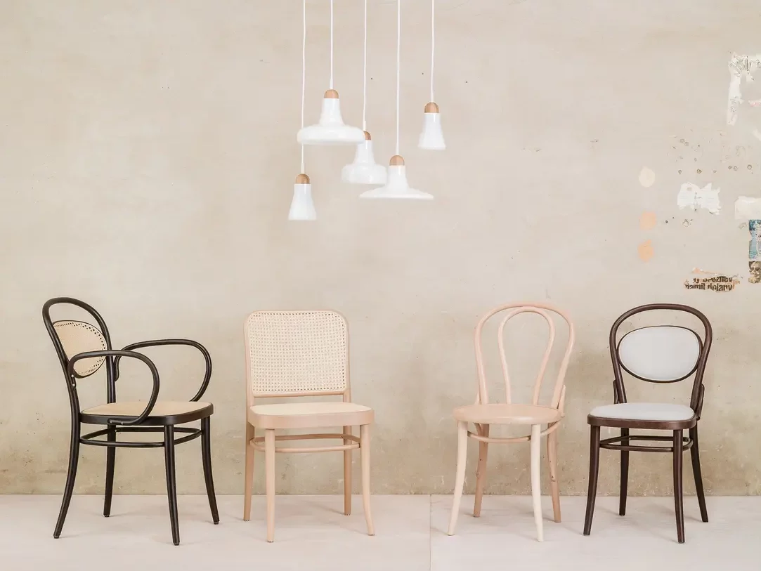 Four diverse styled chairs placed side by side against a textured wall with hanging white pendant lights above.
