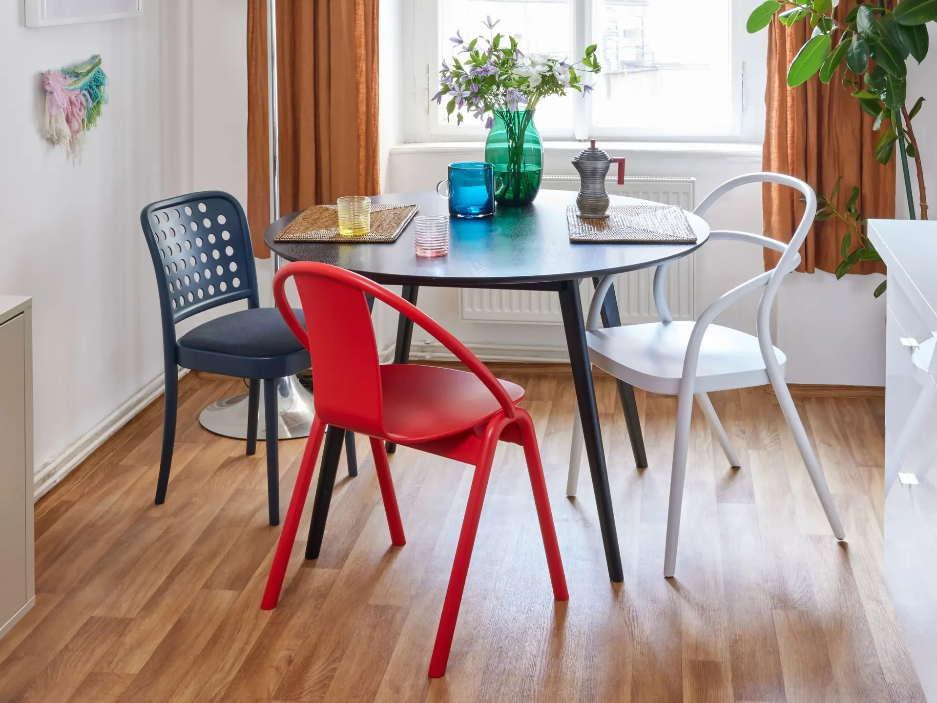 Dining setting with a round table & different colour chairs.