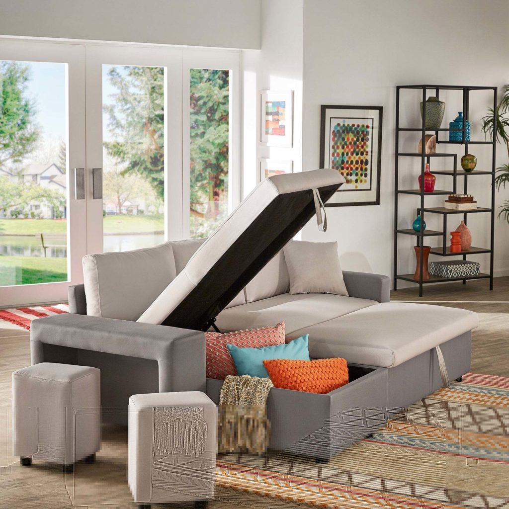 A contemporary living room featuring a spacious gray sectional sofa with an open storage compartment underneath one of its lifted sections. Positioned atop the sofa are vibrant decorative pillows in shades of orange, teal, and patterned designs.