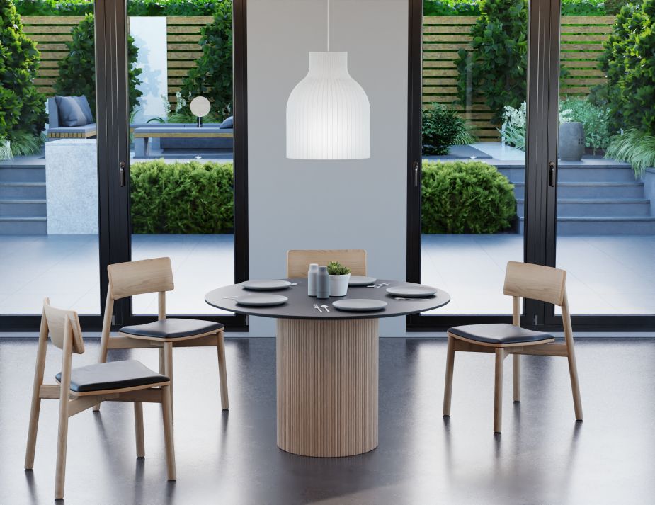 A contemporary dining area with wooden chairs and a table, set against a backdrop of large glass doors that open to a lush garden terrace. A white pendant light hangs above, illuminating the space.




